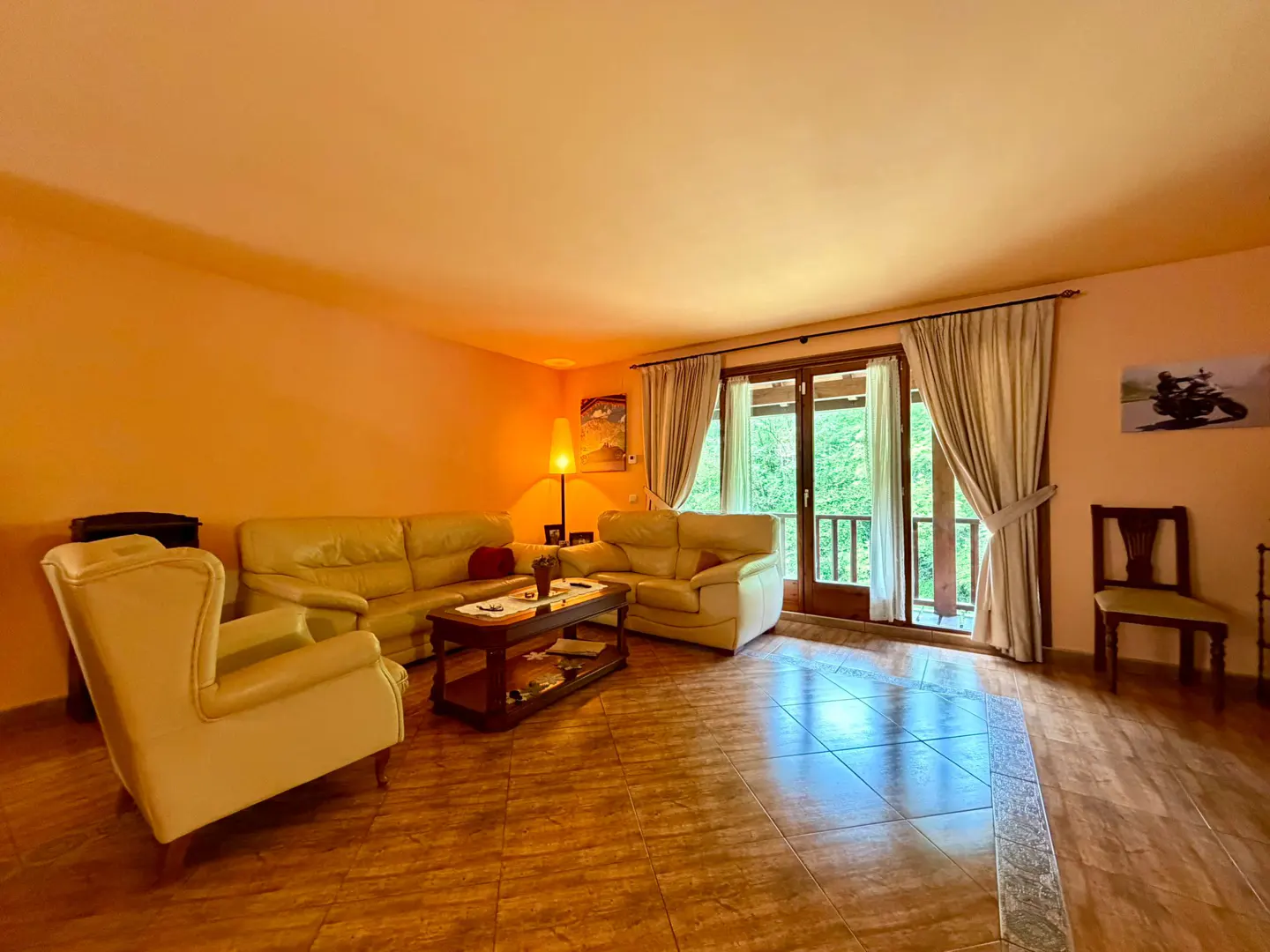 Living room with tile floor, peach walls, cream sofas, and a balcony with green trees visible.