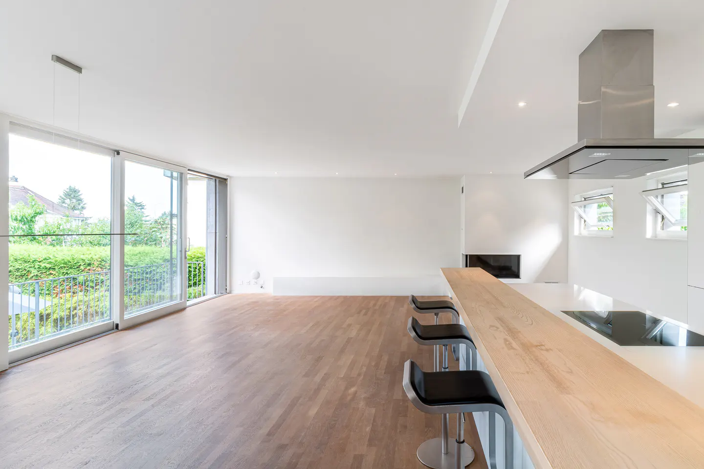 Modern kitchen with light wood breakfast bar, three black stools, hardwood floors, and large sliding glass doors to a patio.