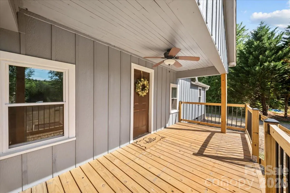 Exterior view of a gray house with a wooden porch, brown door with wreath, and a ceiling fan.