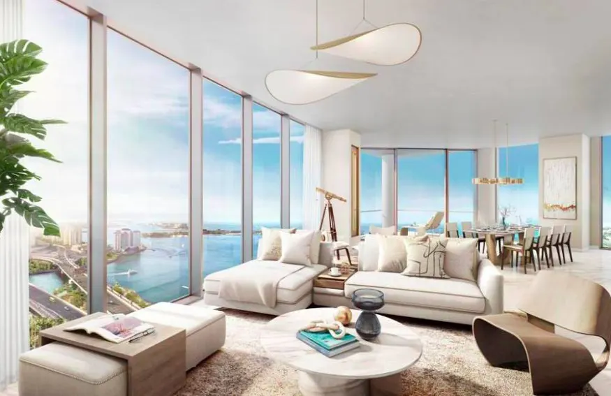 Bright, modern living room with floor-to-ceiling windows overlooking a city and ocean view. White sofas, round table, and dining area.