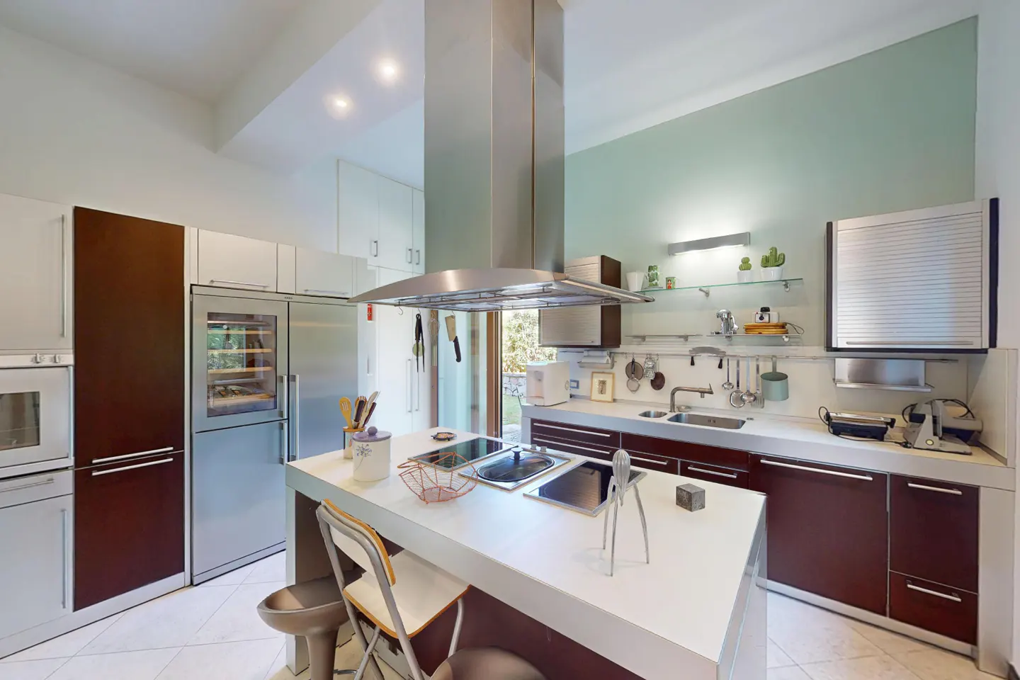 Bright kitchen with white island, stainless steel appliances, and dark wood cabinets. A large window provides natural light.