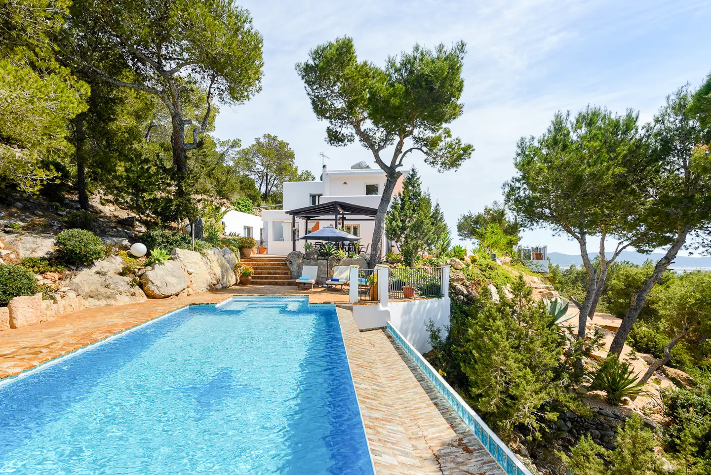 Exterior view of a white house with a pool, trees, and blue sky.