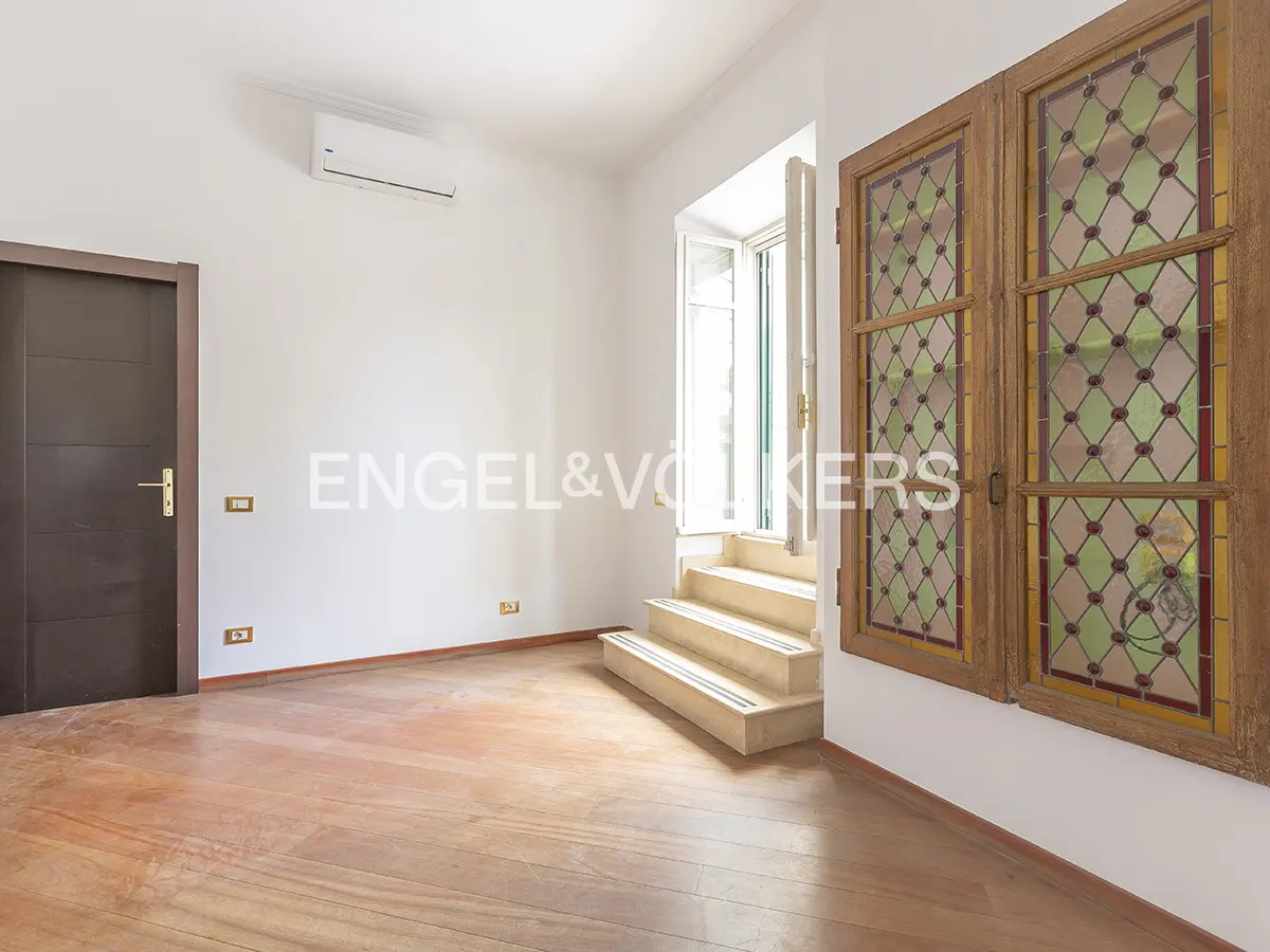 A bright room with hardwood floors, white walls, a dark brown door, and stained glass windows.