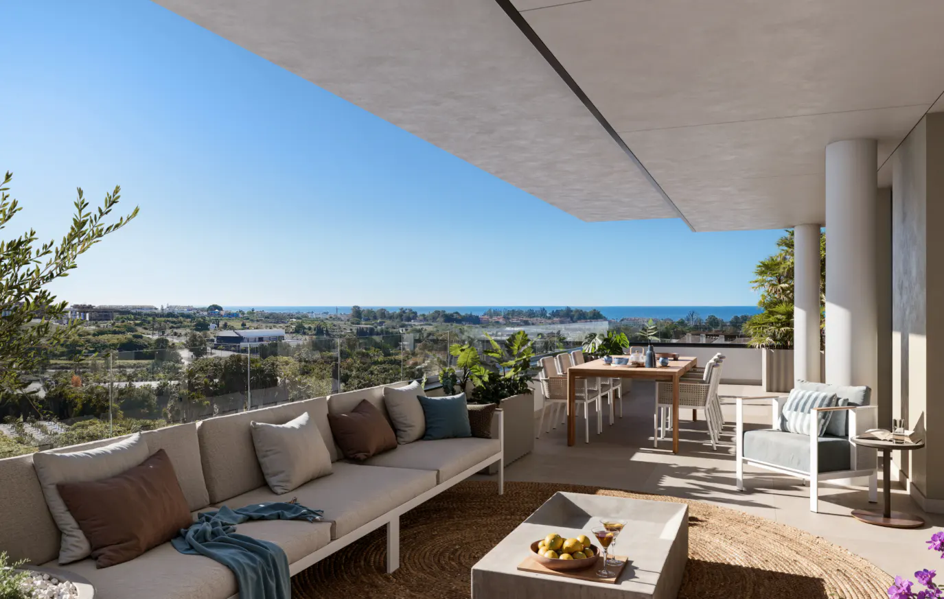 Outdoor patio with a beige sofa, brown pillows, and a blue throw blanket. A dining table and chairs are visible with an ocean view.