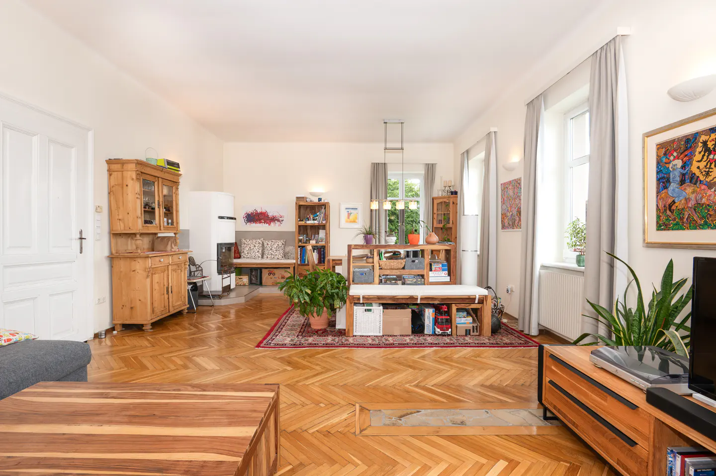 Bright living room with herringbone wood floors, wooden furniture, a white fireplace, and a colorful rug.