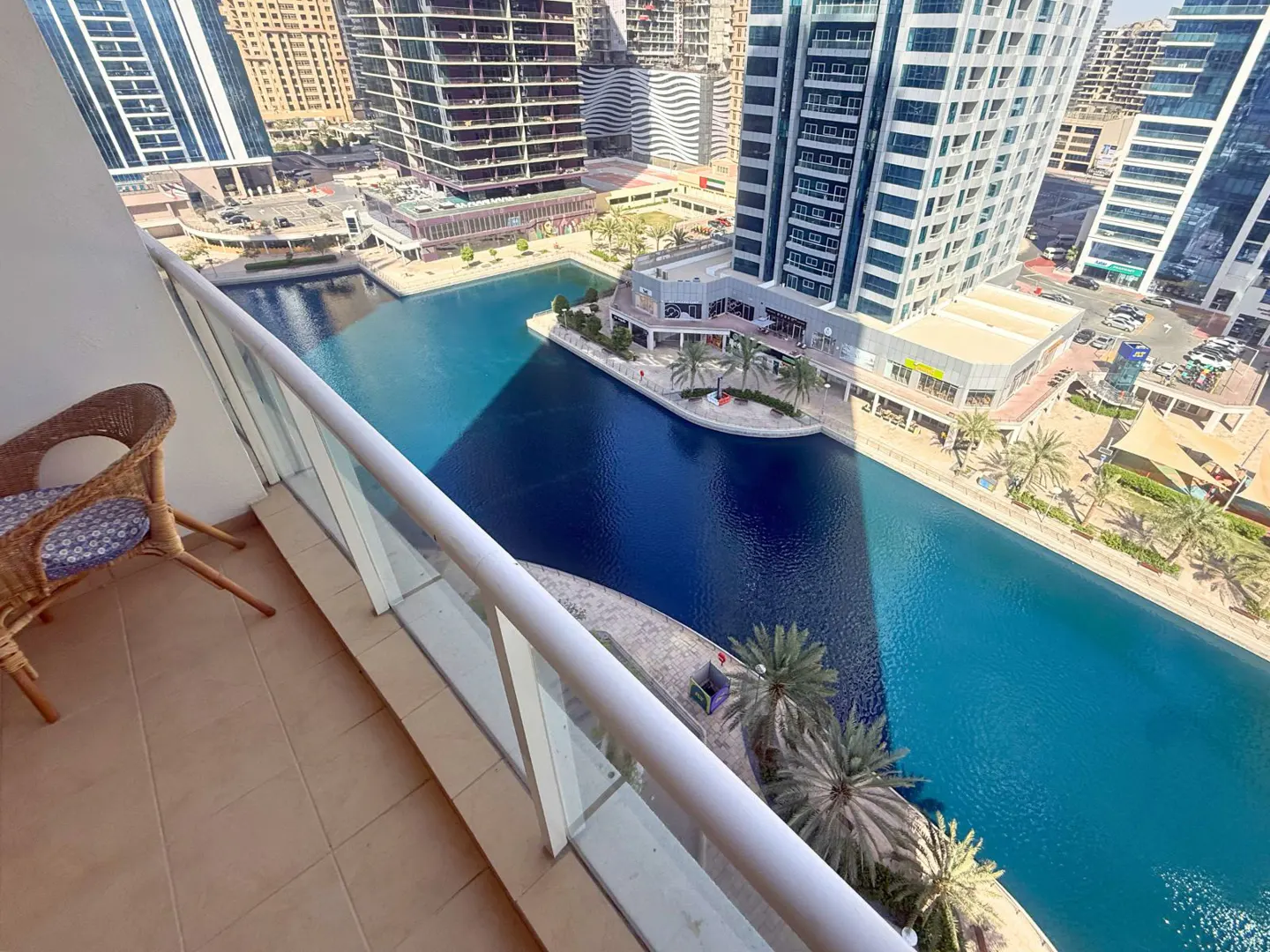 Balcony view of a blue canal surrounded by buildings. A wicker chair sits on the tiled balcony.