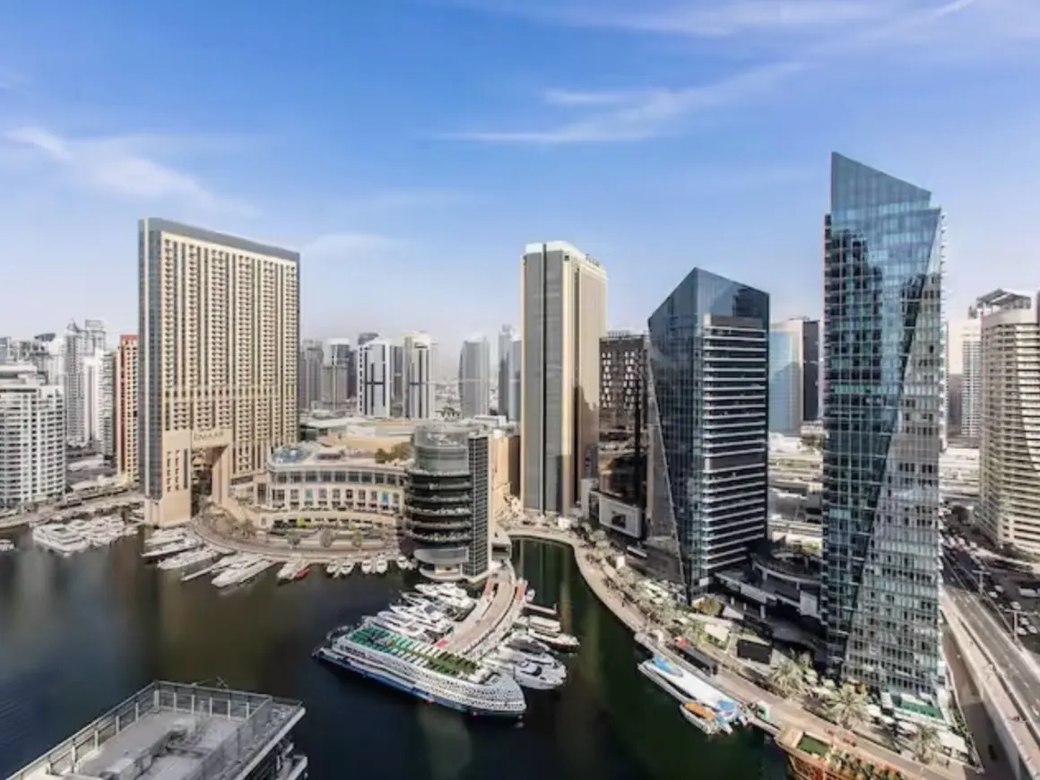 Dubai Marina view with modern high-rise buildings, yachts docked in the harbor, and a clear blue sky.