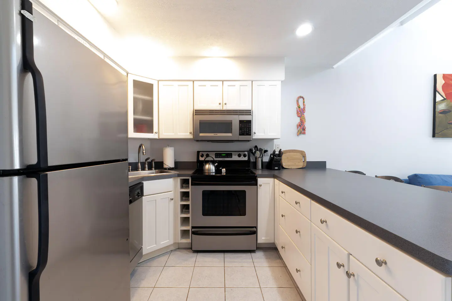 A kitchen with white cabinets, stainless steel appliances, and a gray countertop. A stainless steel refrigerator is on the left.