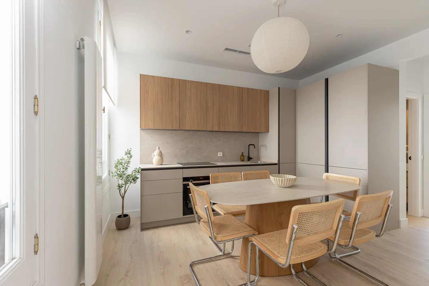 A modern kitchen and dining area with light wood cabinets, a stone table with six chairs, and a white paper lantern.