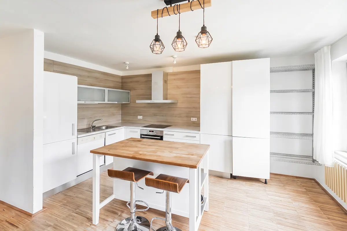 Bright kitchen with white cabinets, wood-look backsplash, and island with two stools. Three pendant lights hang above.