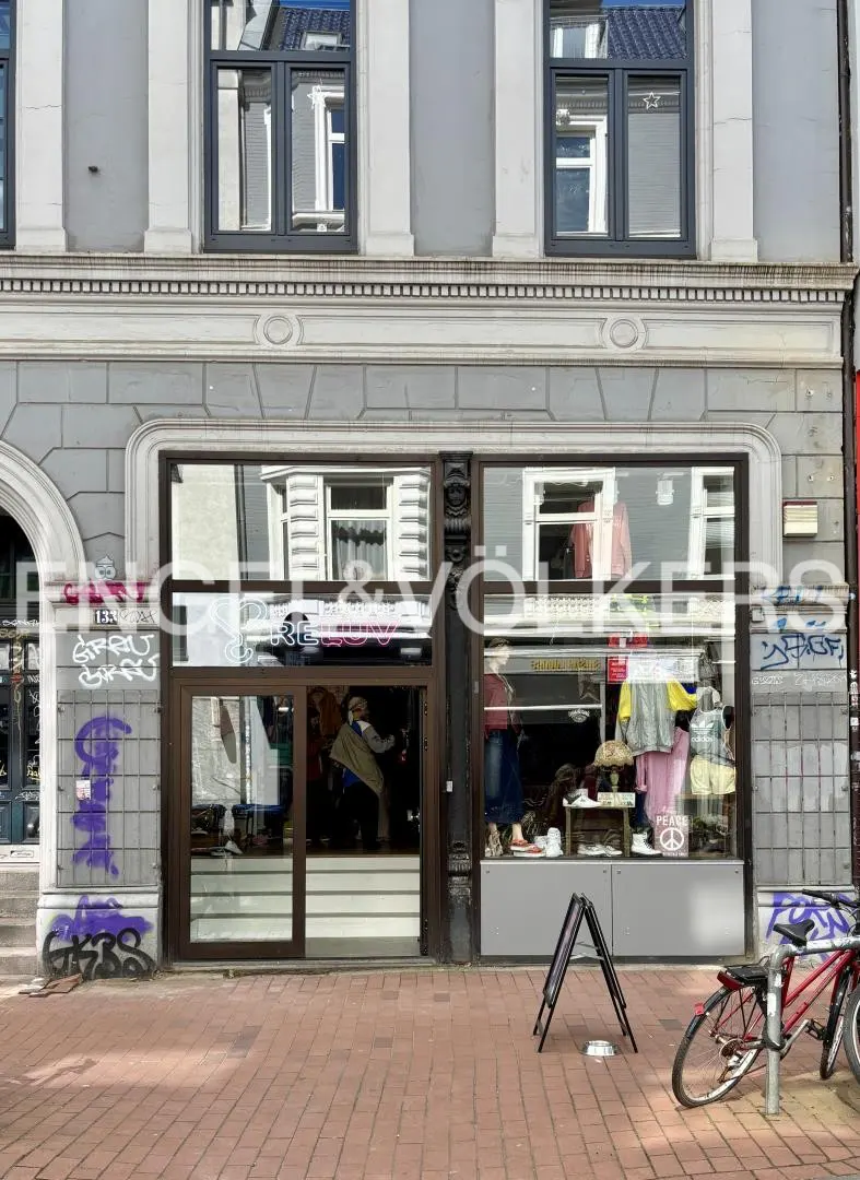 Storefront with large glass windows displaying clothing, grey stone facade with graffiti, and a bicycle on the sidewalk.