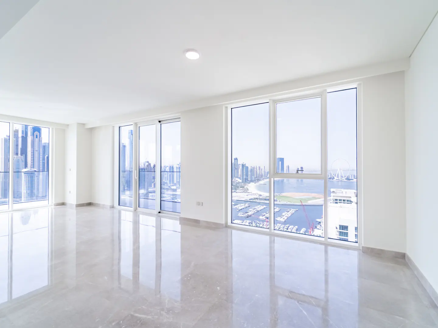 Bright, empty room with white walls, polished marble floors, and floor-to-ceiling windows overlooking a city marina.
