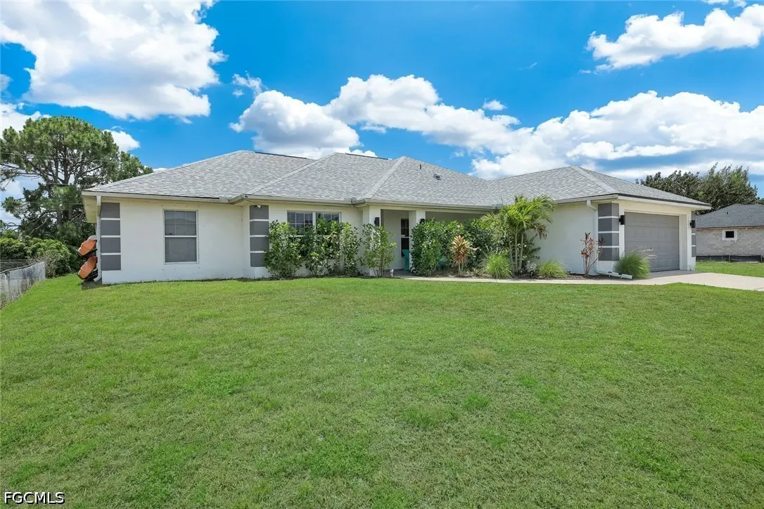 A white, single-story house with a gray roof and a large green lawn under a blue sky with white clouds.