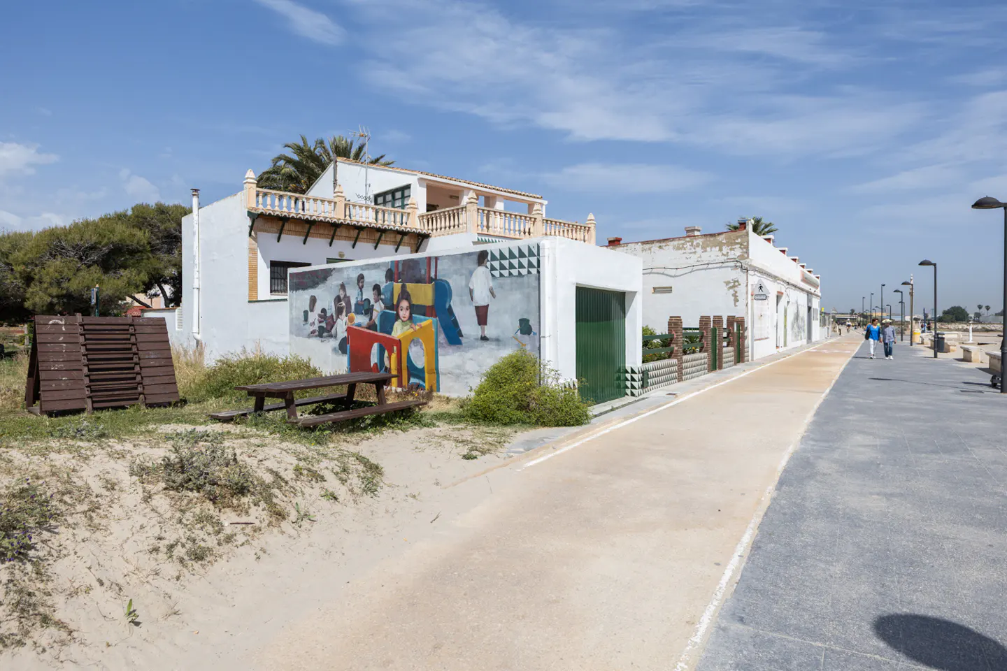 Exterior view of a white building with a mural of children playing, a picnic table, and a walkway.