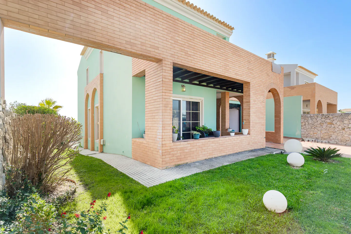 Exterior view of a two-story home with a light green facade and brick accents, surrounded by a green lawn and landscaping.