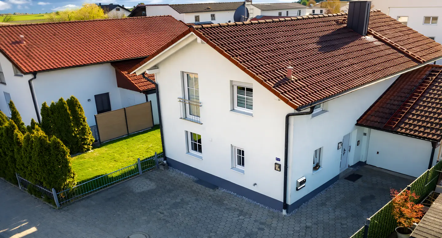 Aerial view of a two-story white house with a red tile roof and a gray brick driveway.