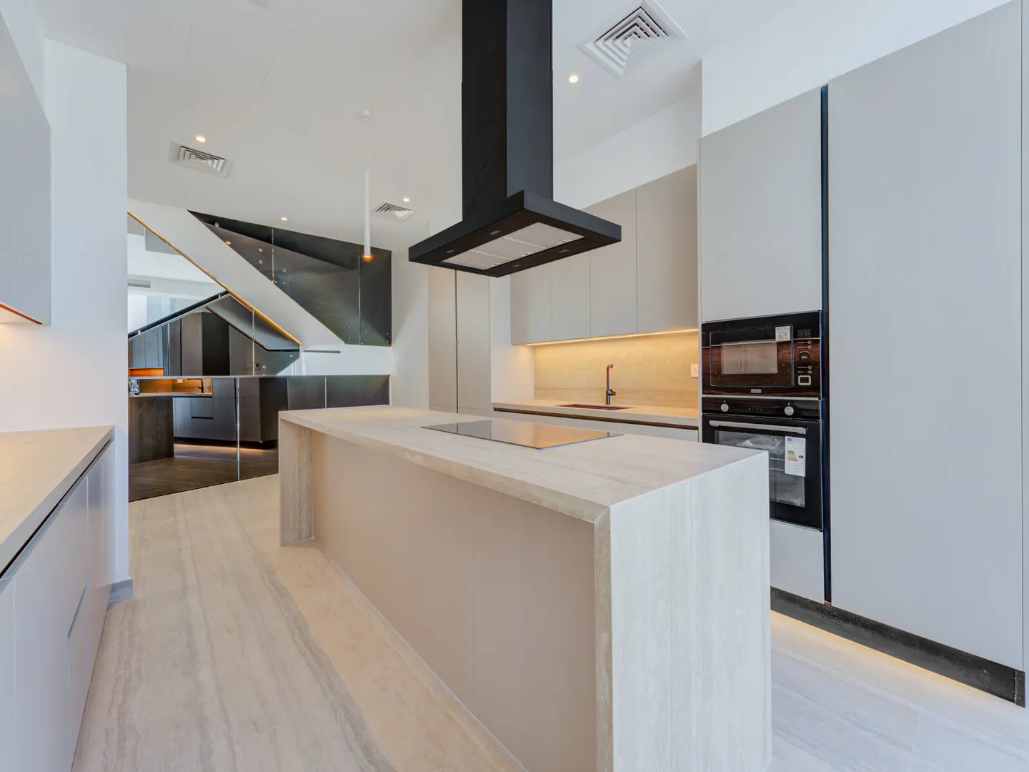 Modern kitchen with a large island, black range hood, and built-in oven. Gray cabinets and marble floors create a sleek design.