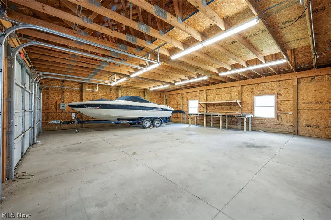 A large garage with a boat on a trailer, wood walls, and a concrete floor.