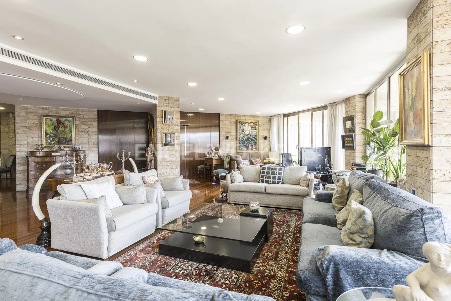 Spacious living room with gray sofas, a black coffee table on a patterned rug, and artwork on stone walls.
