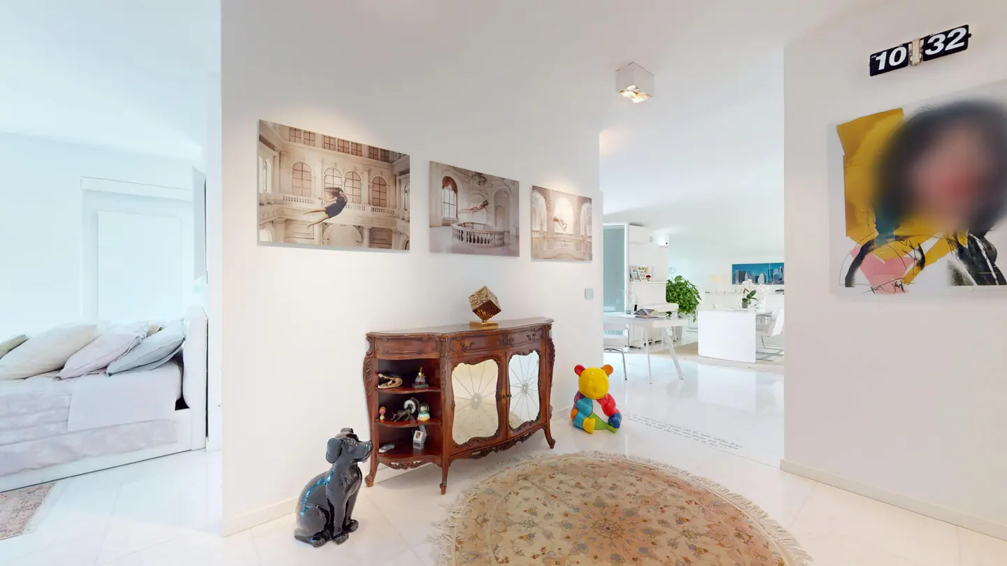 Bright, white hallway with art. Three ballerina prints hang above a wooden cabinet. A black dog statue sits nearby. A colorful bear and round rug add charm.