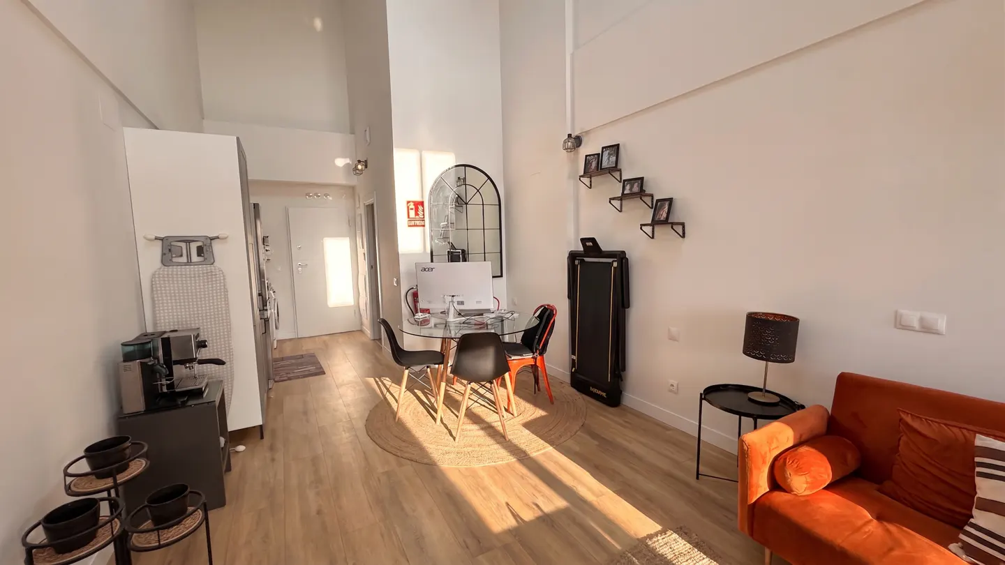Bright, modern apartment interior with wood floors, orange sofa, glass table with chairs, and white walls.