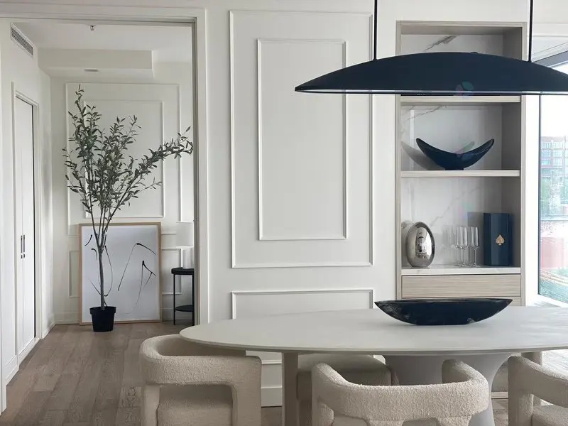 Modern dining room with oval table, cream textured chairs, built-in shelving, and a large black pendant light.