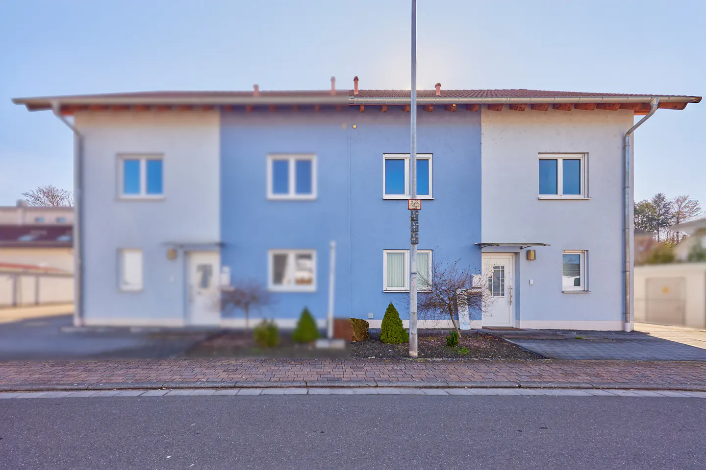 A two-story duplex with white and blue exterior walls, white-framed windows, and two front entrances under a tiled roof.
