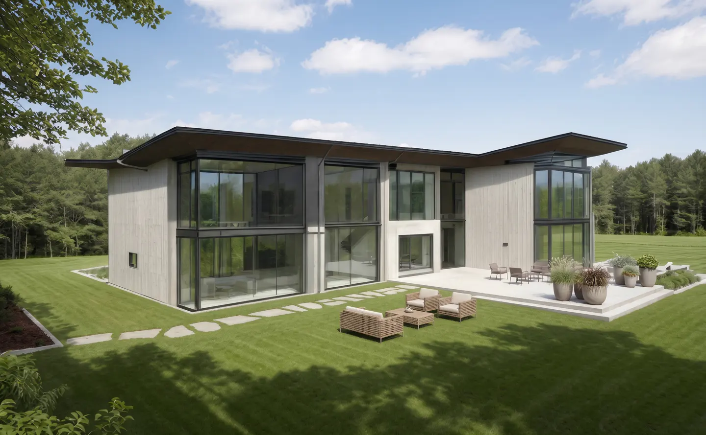 Modern two-story home with large windows, a patio with seating, and a green lawn. Trees and blue sky in the background.