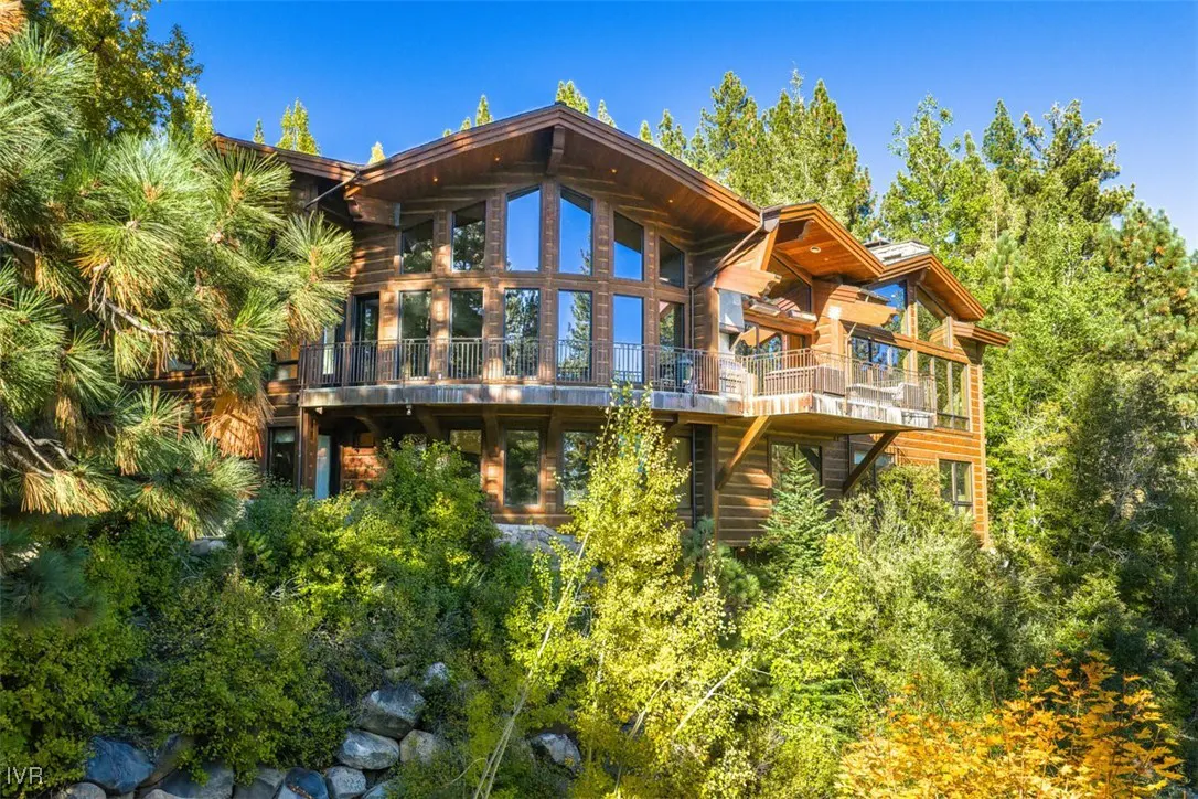 A large, multi-story log cabin with balconies, surrounded by lush green trees and a blue sky.