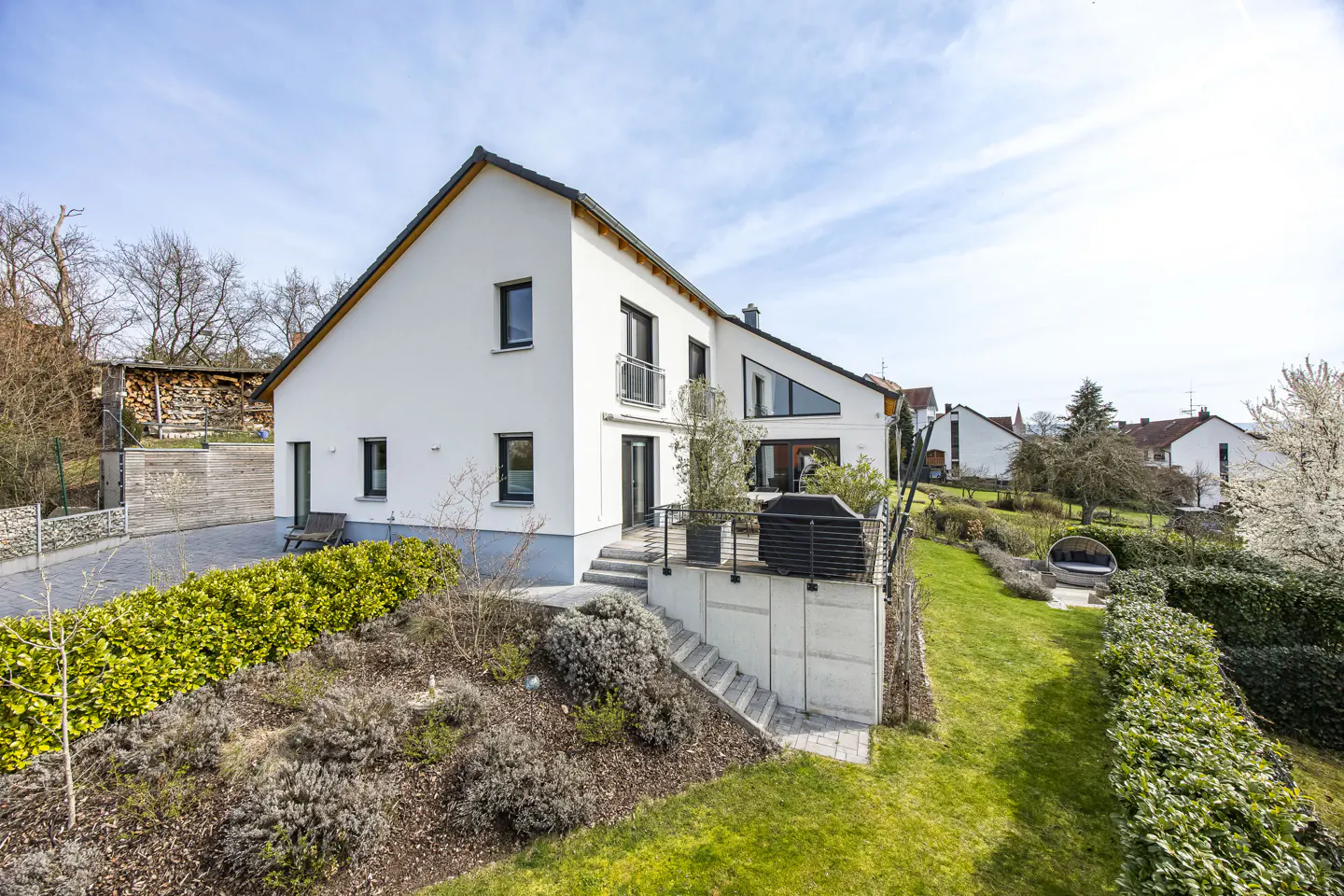 Modern white house with a black roof, balcony, and a green lawn on a sunny day.