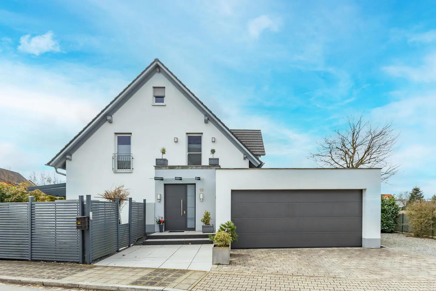 Two-story white house with a gray roof, gray door, and gray garage door under a blue sky.