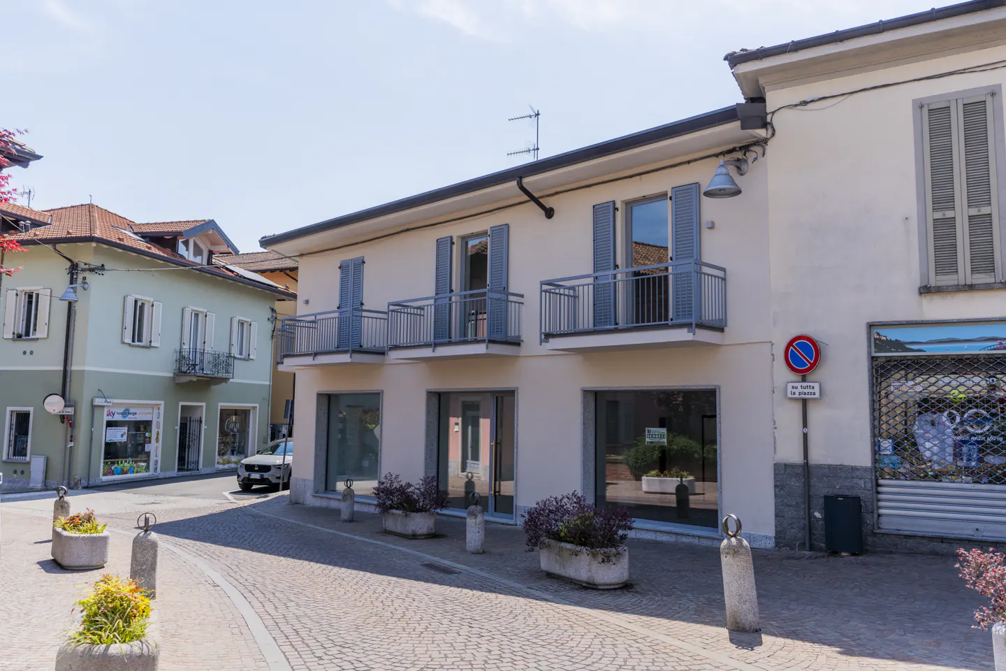 Two-story cream building with blue shutters and balconies, on a cobblestone street with flower planters.