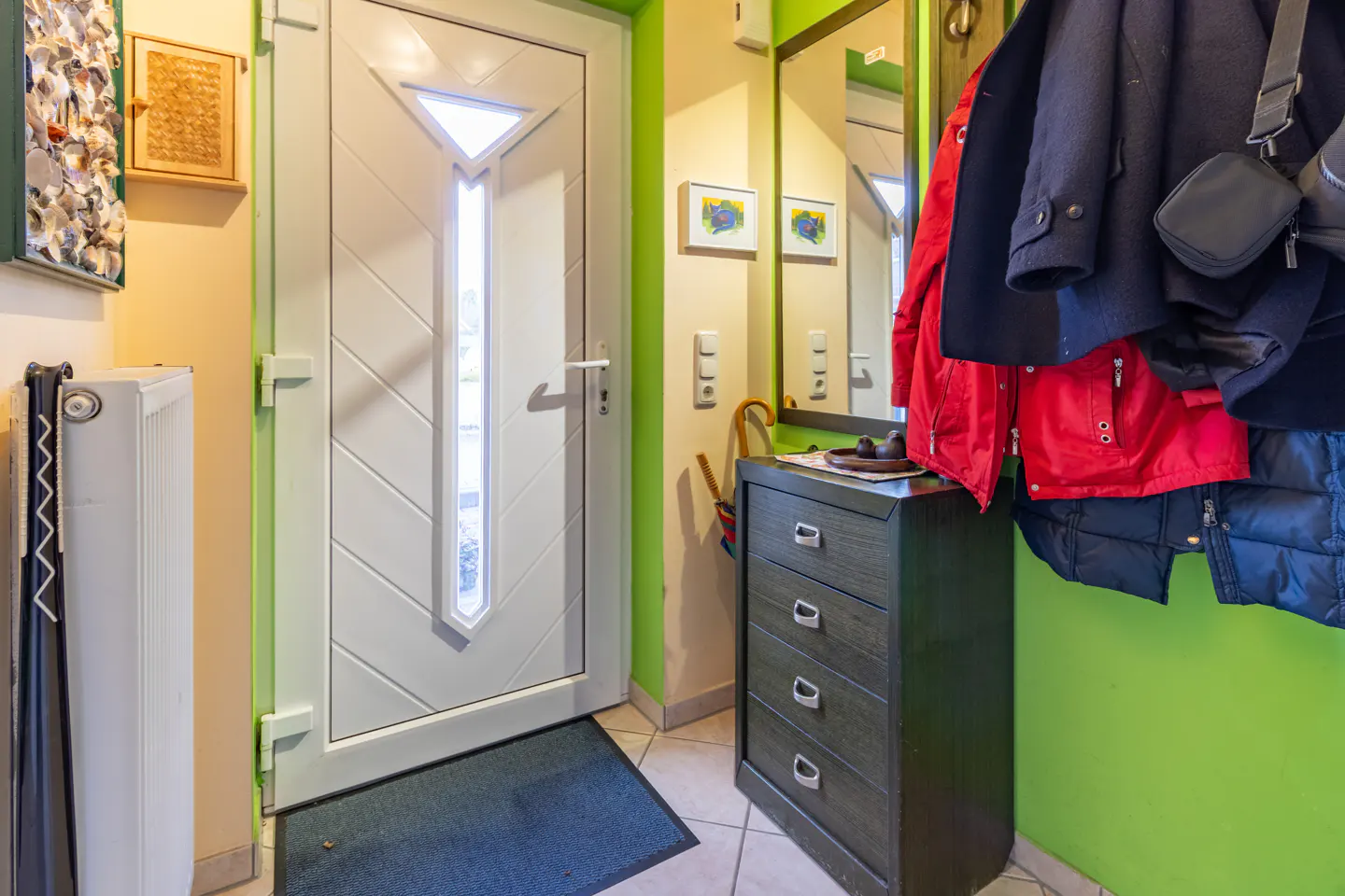 Entryway with a white door, a dark wood dresser, and coats hanging on a green wall.