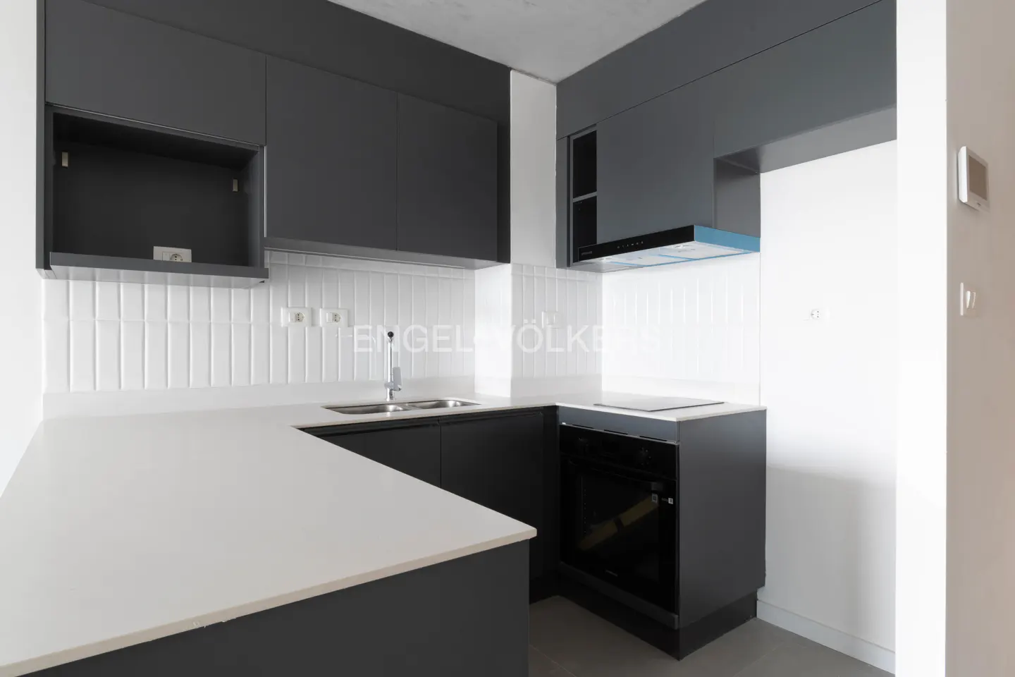 Modern kitchen with dark grey cabinets, white countertops, white subway tile backsplash, and built-in black appliances.
