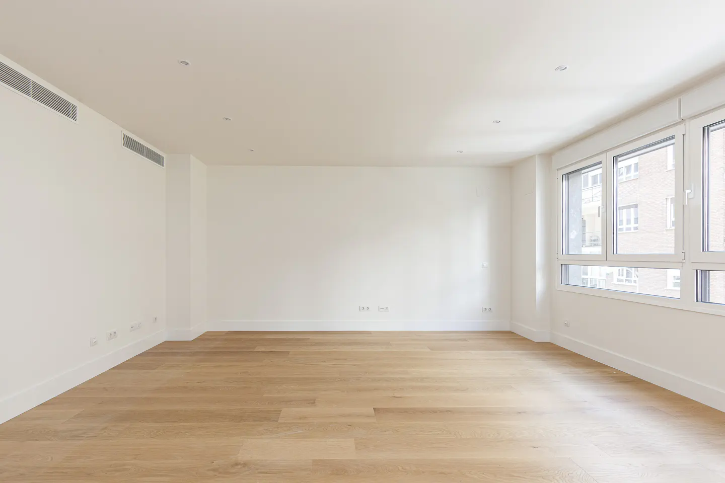 Bright, empty room with light wood floors, white walls, and large windows.