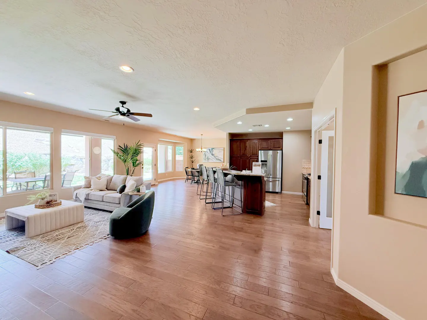 Open-concept living space with hardwood floors, a kitchen island with bar stools, and a living room with a gray sofa and large windows.