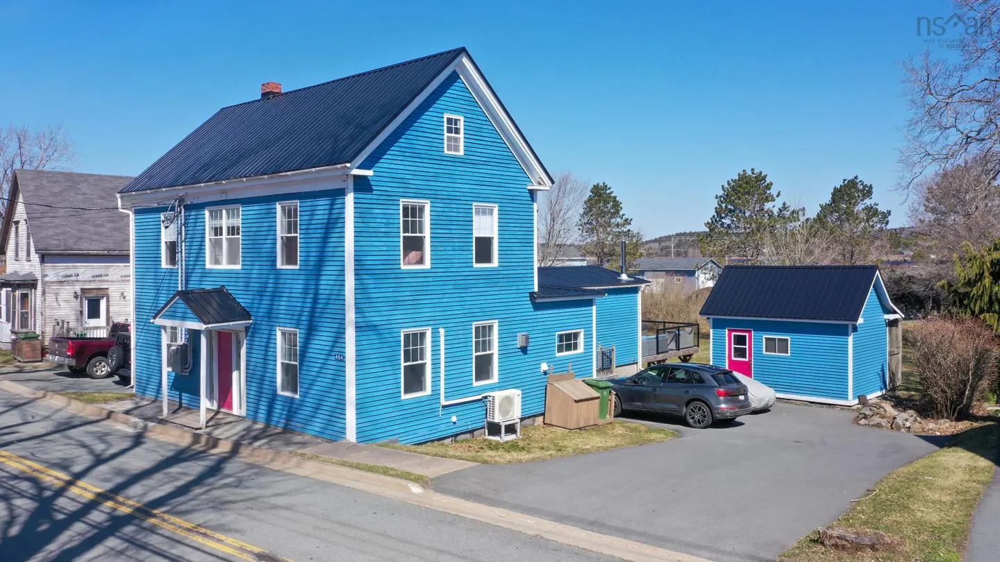 Two-story blue house with a black roof and a pink front door, with a matching shed and a gray car in the driveway.