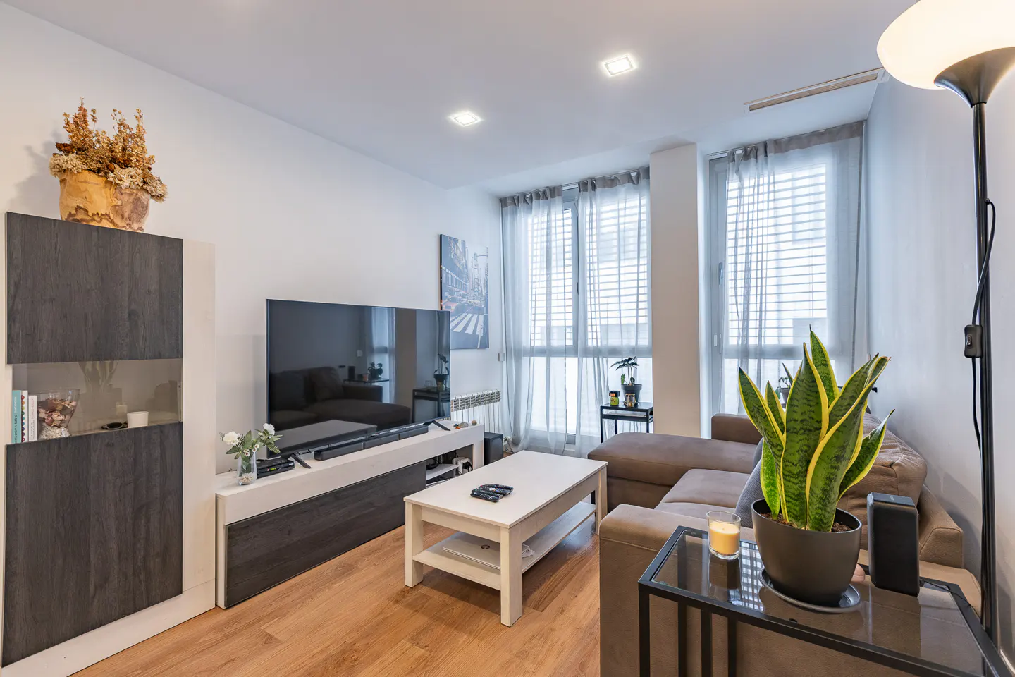 Living room with wood floors, a brown sectional sofa, a white coffee table, and a large TV with a gray media console.