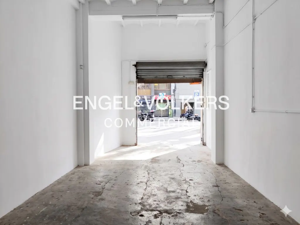 Interior view of a commercial space with white walls and a concrete floor, looking out to a street scene with motorcycles.
