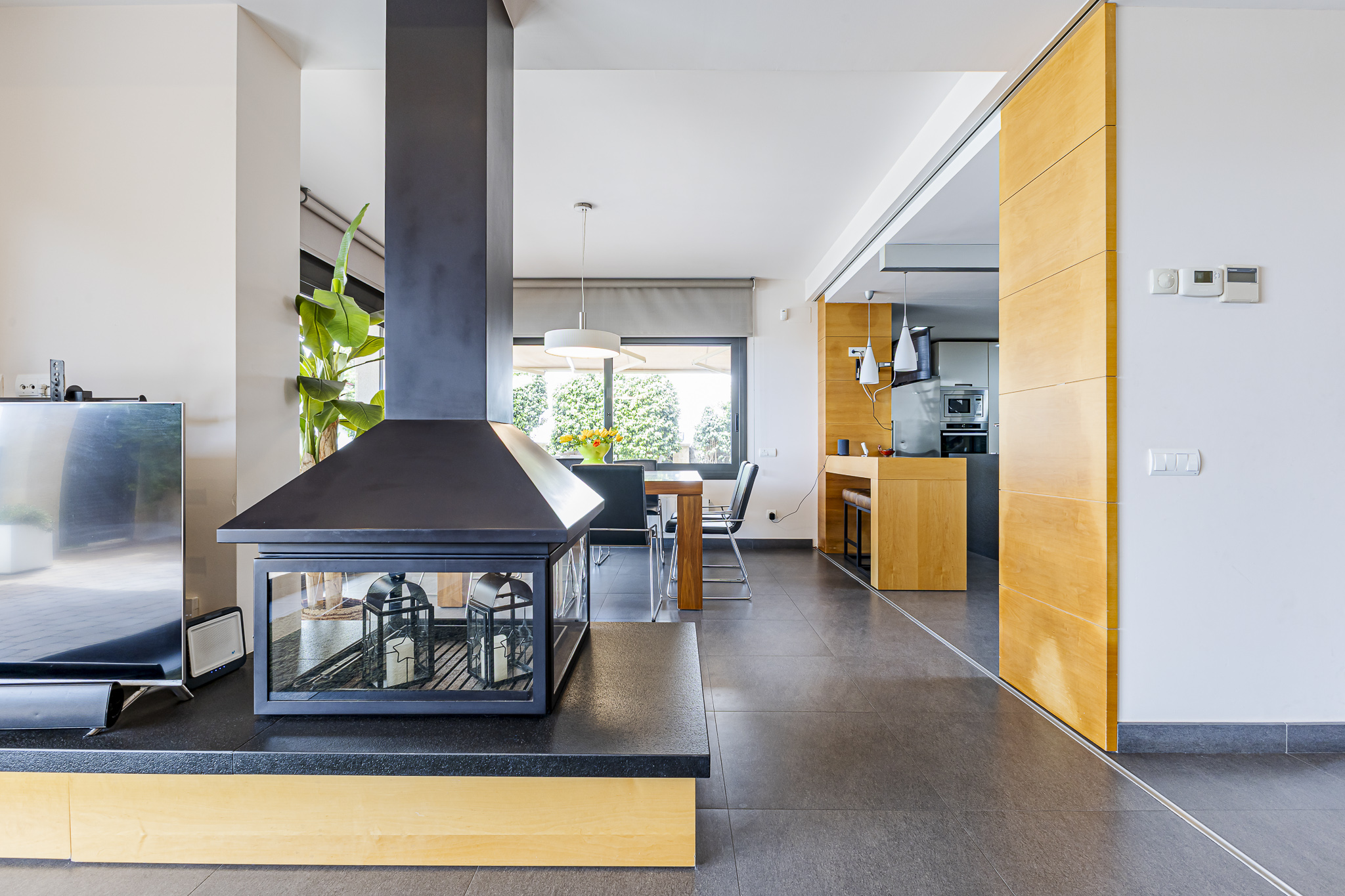 Modern living room with a black fireplace, tiled floors, and a view into a wooden-accented kitchen and dining area.