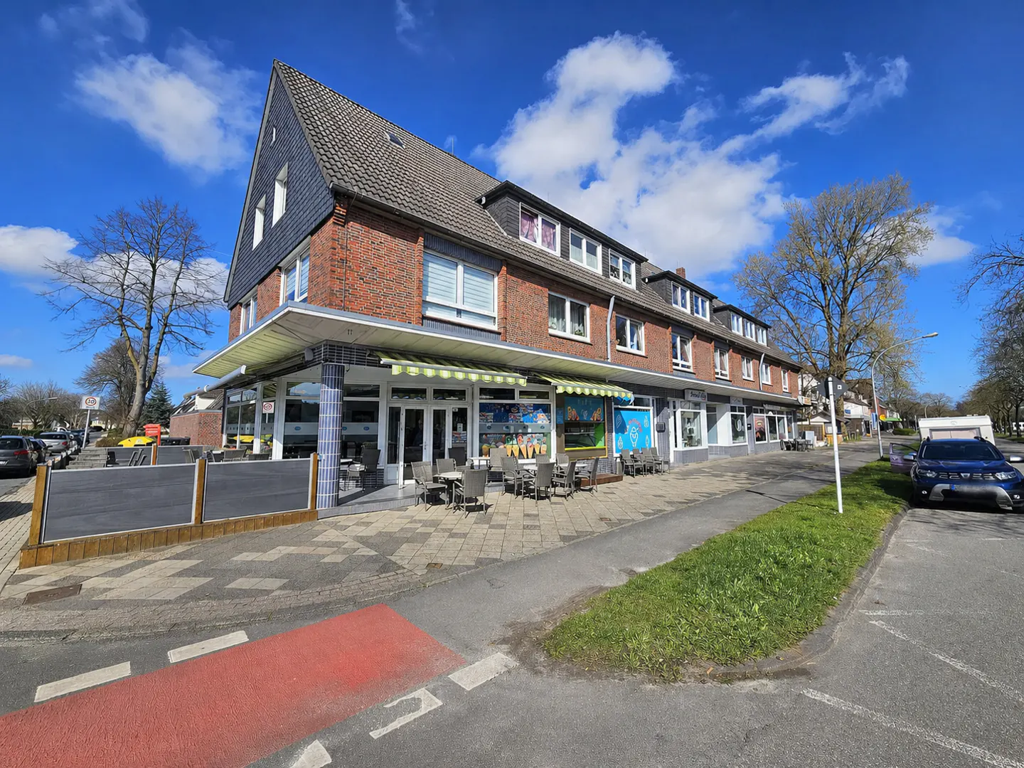 A two-story brick building with shops and a restaurant on the ground floor. Tables and chairs are set up outside.