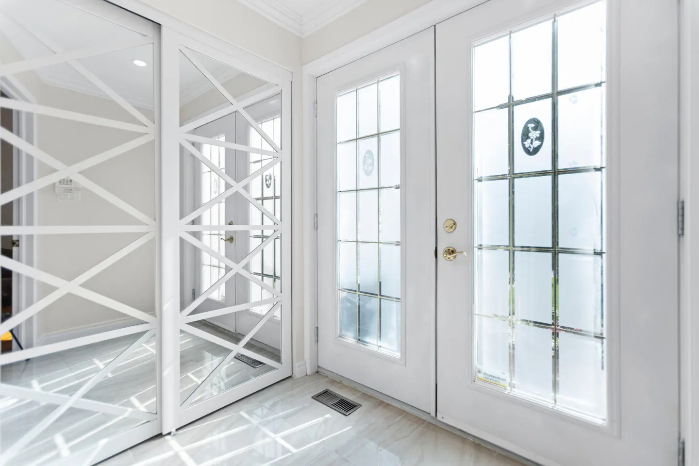 Bright foyer with white doors and geometric mirrored closet doors. Marble flooring reflects light.