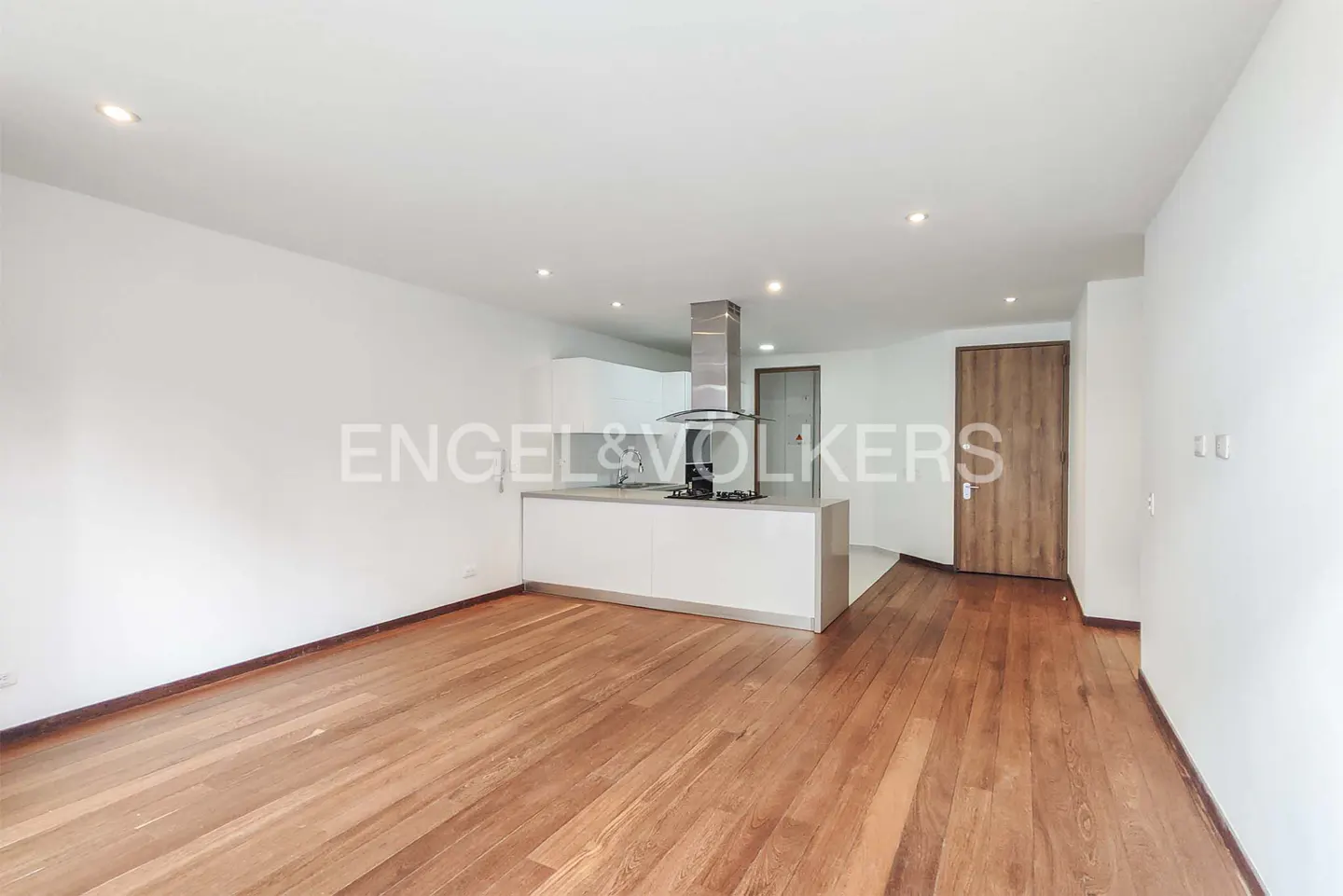 Modern open-plan kitchen with white cabinets, stainless steel hood, and hardwood floors in a bright, minimalist room.