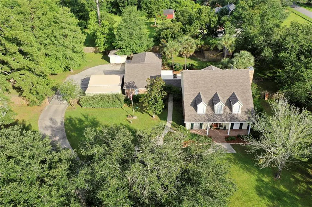 Aerial view of a two-story home with a brown roof, dormer windows, and a long driveway surrounded by lush green trees.