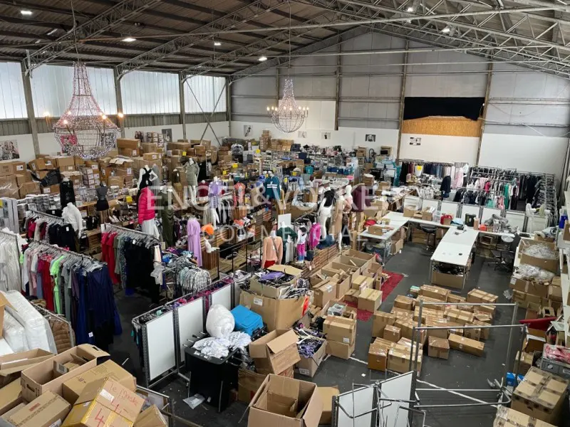 Overhead shot of a large warehouse space filled with clothing racks, mannequins, and cardboard boxes. Chandeliers hang from the ceiling.