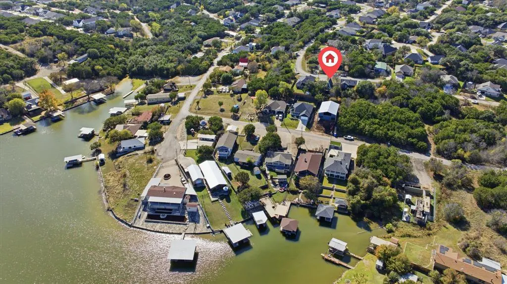 Aerial view of waterfront homes with boat docks on a lake surrounded by green trees, with a red house icon.