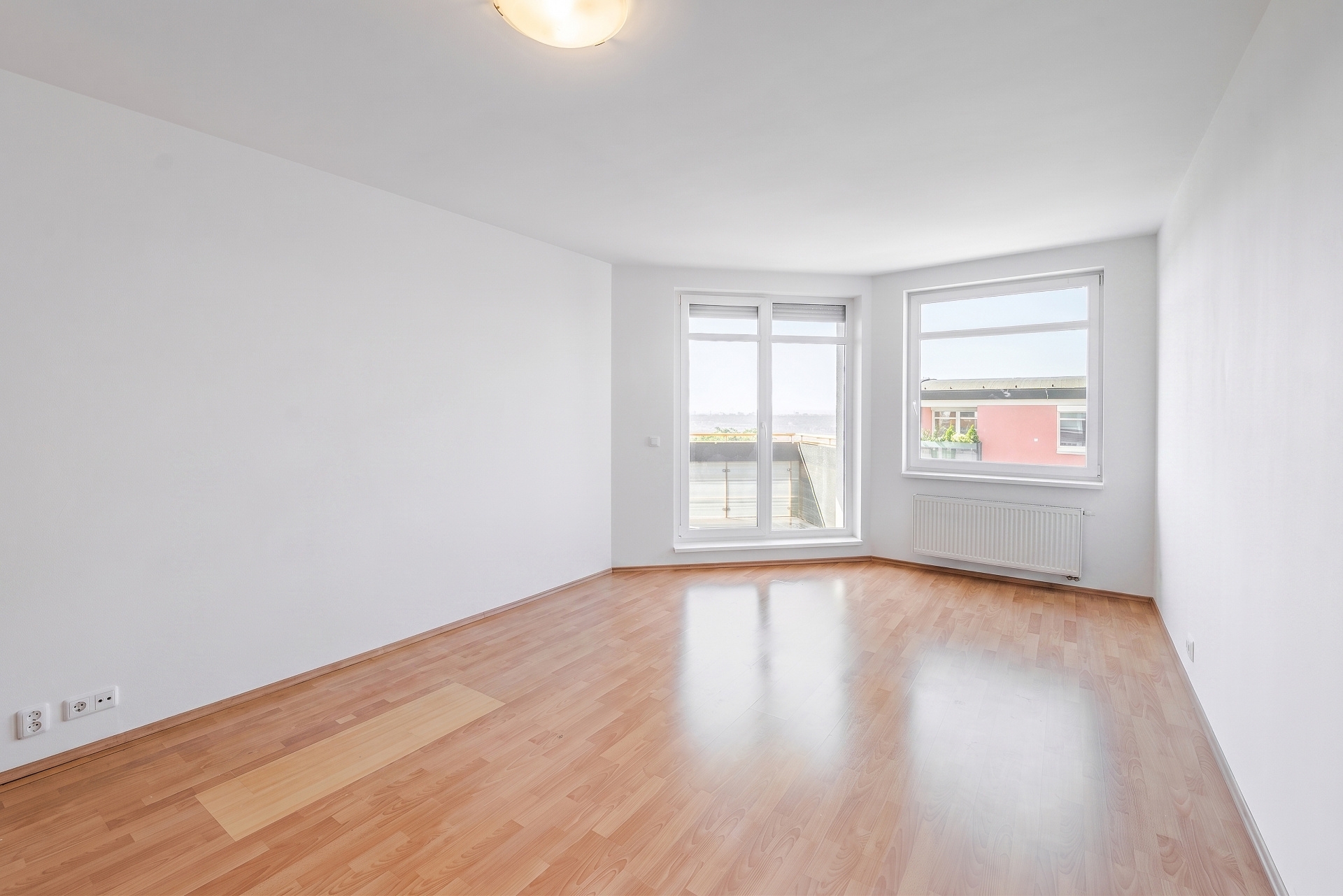 Empty room with white walls, light wood flooring, a large window, and a glass door leading to a balcony.