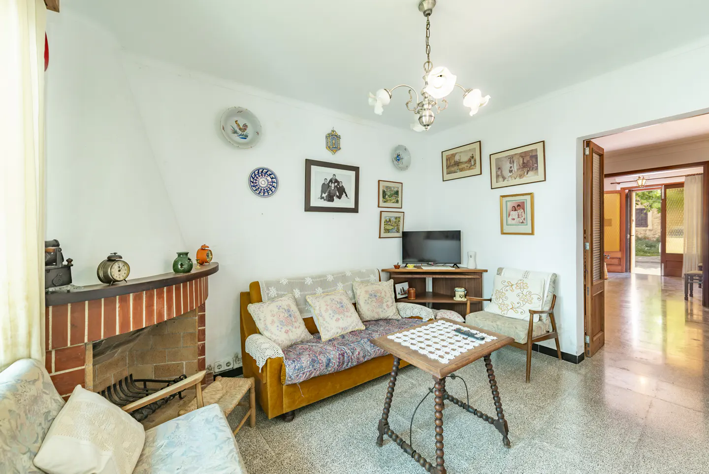 Cozy living room with a brick fireplace, yellow sofa, wooden coffee table, and walls decorated with framed photos and plates.