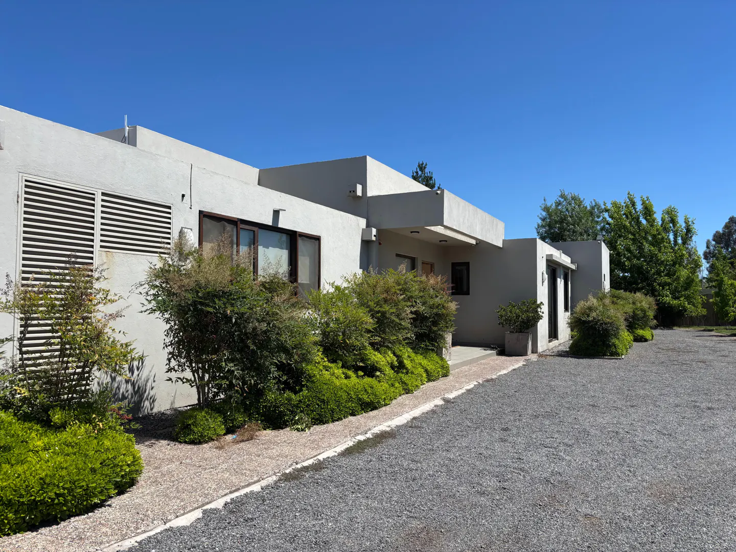 Exterior of a modern, one-story white building with a gravel driveway and green landscaping under a clear blue sky.
