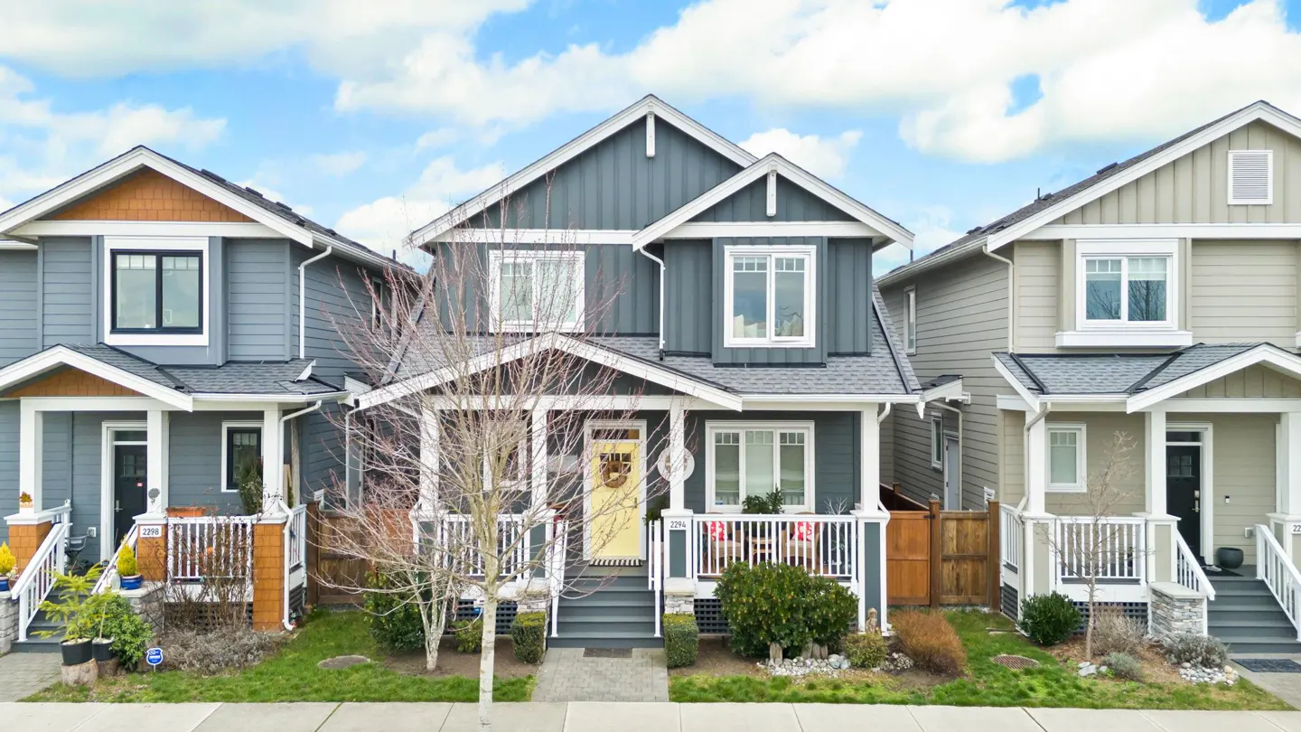 Two-story gray house with a yellow door, white trim, and a small front porch. Neighboring houses are visible on either side.
